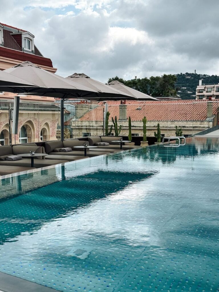 Rooftop infinity pool at Five Seas Hotel Cannes with lounge seating and umbrellas overlooking the city rooftops