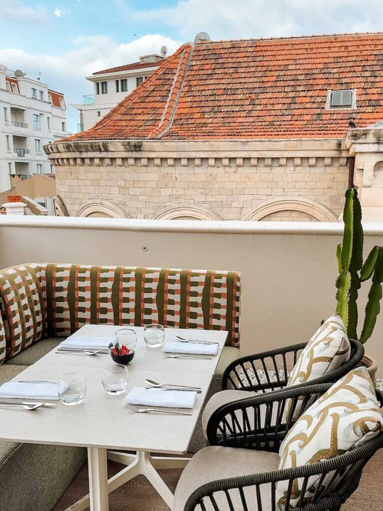 Outdoor rooftop dining table at Le Roof with patterned cushions and views over Cannes rooftops