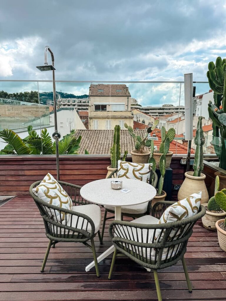 Rooftop seating area at Le Roof with round table woven chairs cactus plants and Cannes city views