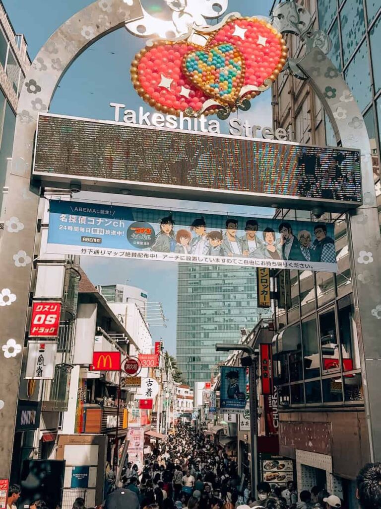 Crowded Takeshita Street in Harajuku Tokyo viewed from above with the iconic entrance arch and colorful signs lining the narrow shopping street