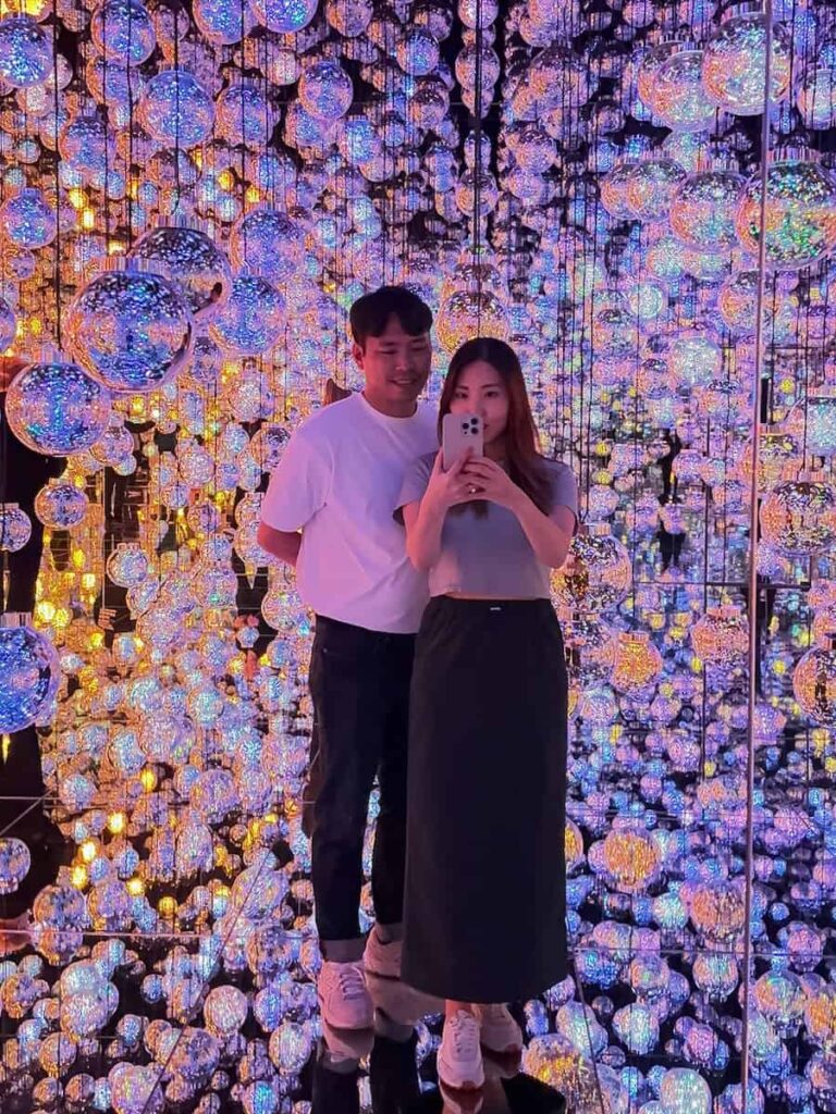 Couple taking a mirror photo inside teamLab Borderless in Tokyo surrounded by hanging crystal light spheres creating an immersive digital art experience