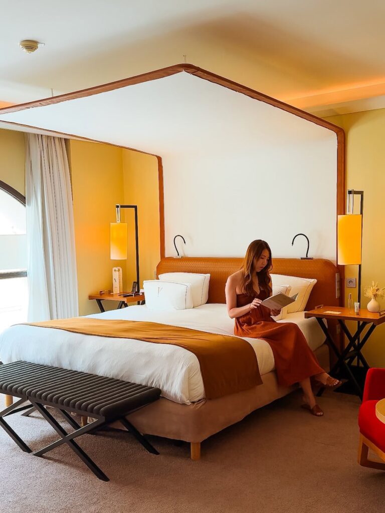 Woman sitting on a hotel bed at Five Seas Hotel Cannes enjoying a quiet moment inside a boutique luxury room