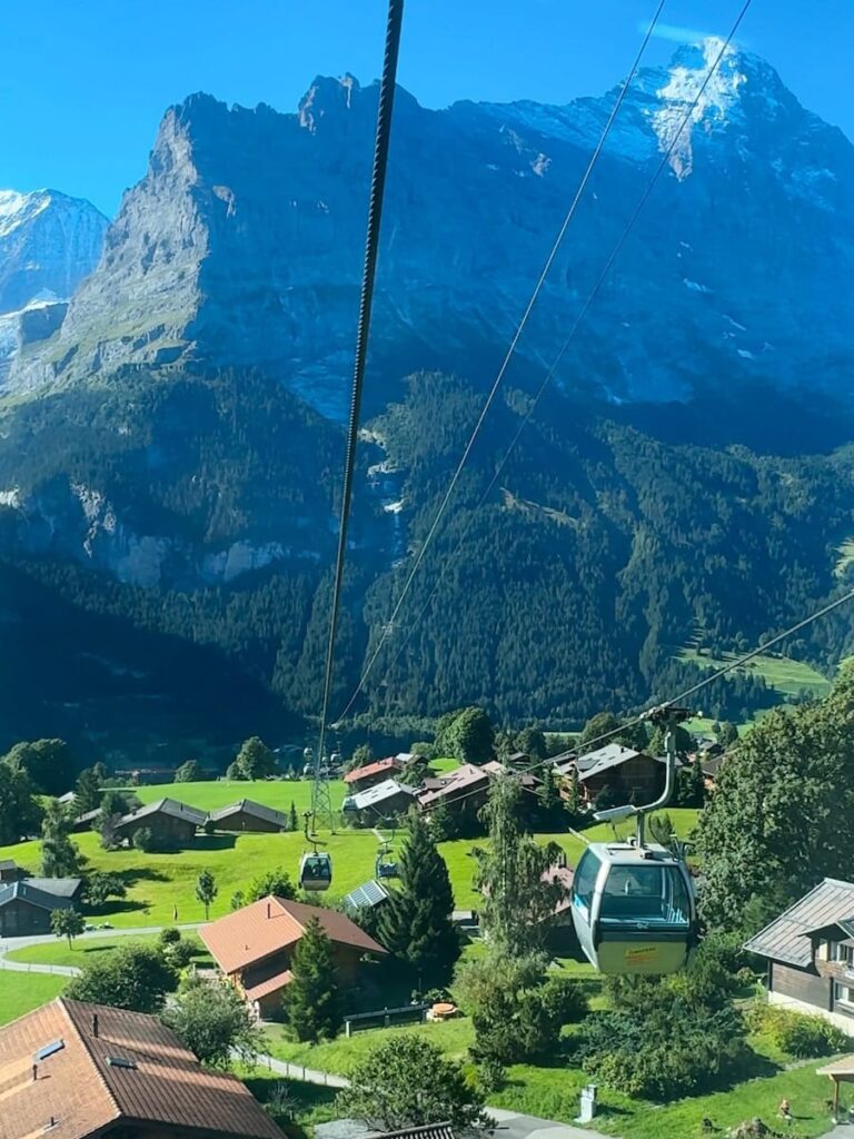 Grindelwald First gondola cabins soaring above alpine village and green valleys with Eiger mountain backdrop in Switzerland