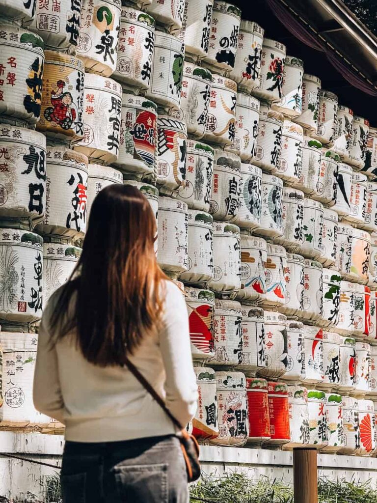 Visitor standing in front of stacked sake barrels at Meiji Shrine in Tokyo showcasing traditional Japanese rice wine offerings and cultural details