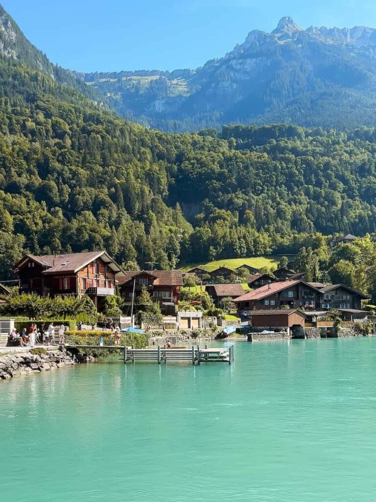Turquoise Lake Brienz surrounded by traditional Swiss chalets, lush green forests, and mountains on a sunny day in Switzerland.