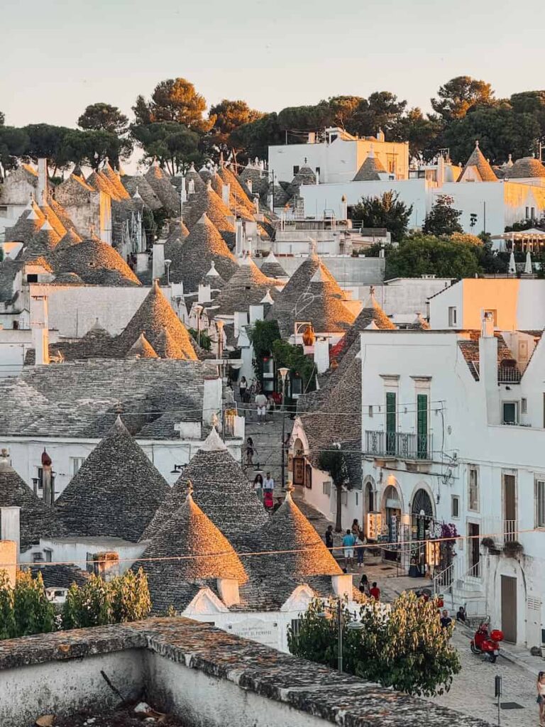 Panoramic view of Alberobello at golden hour, showcasing hundreds of traditional trulli with conical stone roofs stretching across the UNESCO World Heritage town in Puglia, Italy.