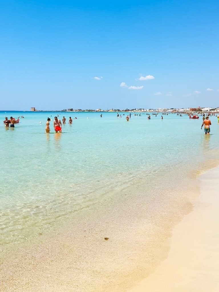 Crystal clear shallow turquoise water at Porto Cesareo, where visitors wade through calm Caribbean-like water along one of Puglia's most beautiful sandy beaches.