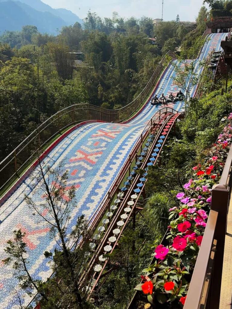 Visitors riding the rainbow slide at Cat Cat Village near Sapa, Vietnam, with colorful lanes winding through lush mountain scenery.