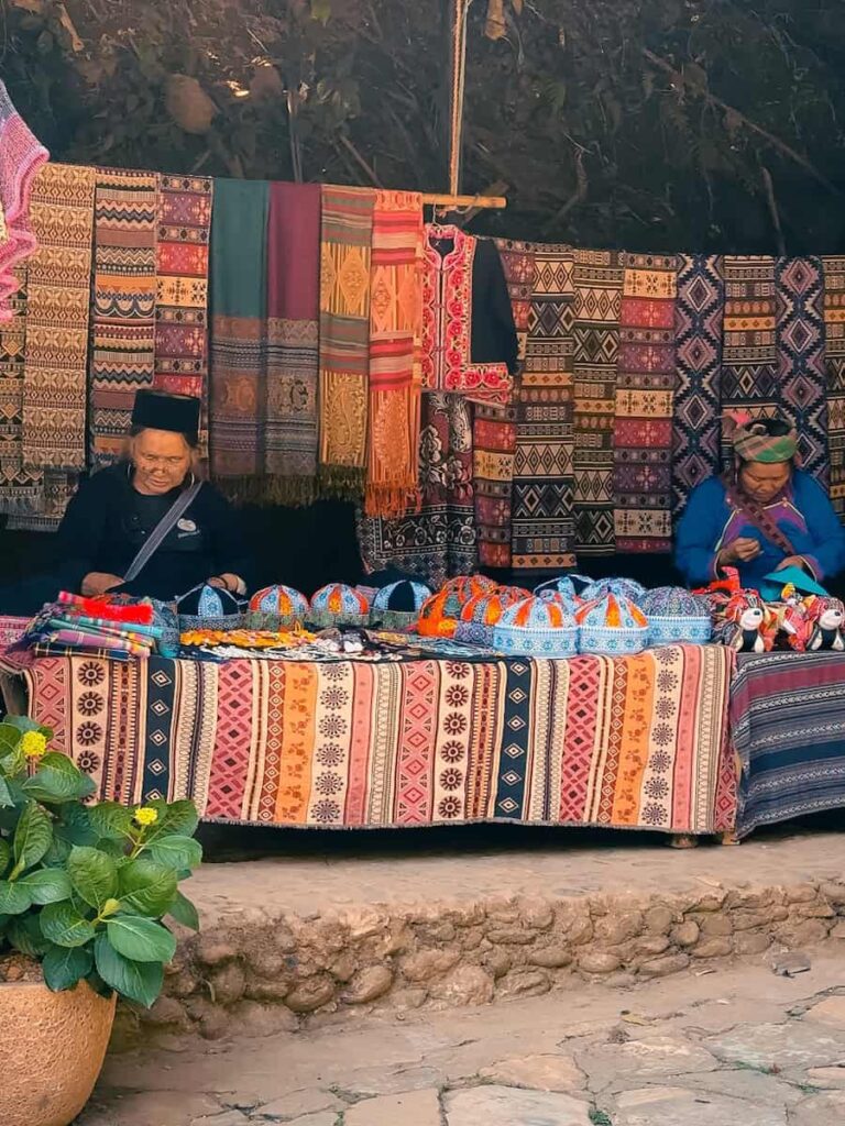 Local women selling handmade textiles, embroidered fabrics, and traditional crafts at a market stall in Cat Cat Village near Sapa, Vietnam.
