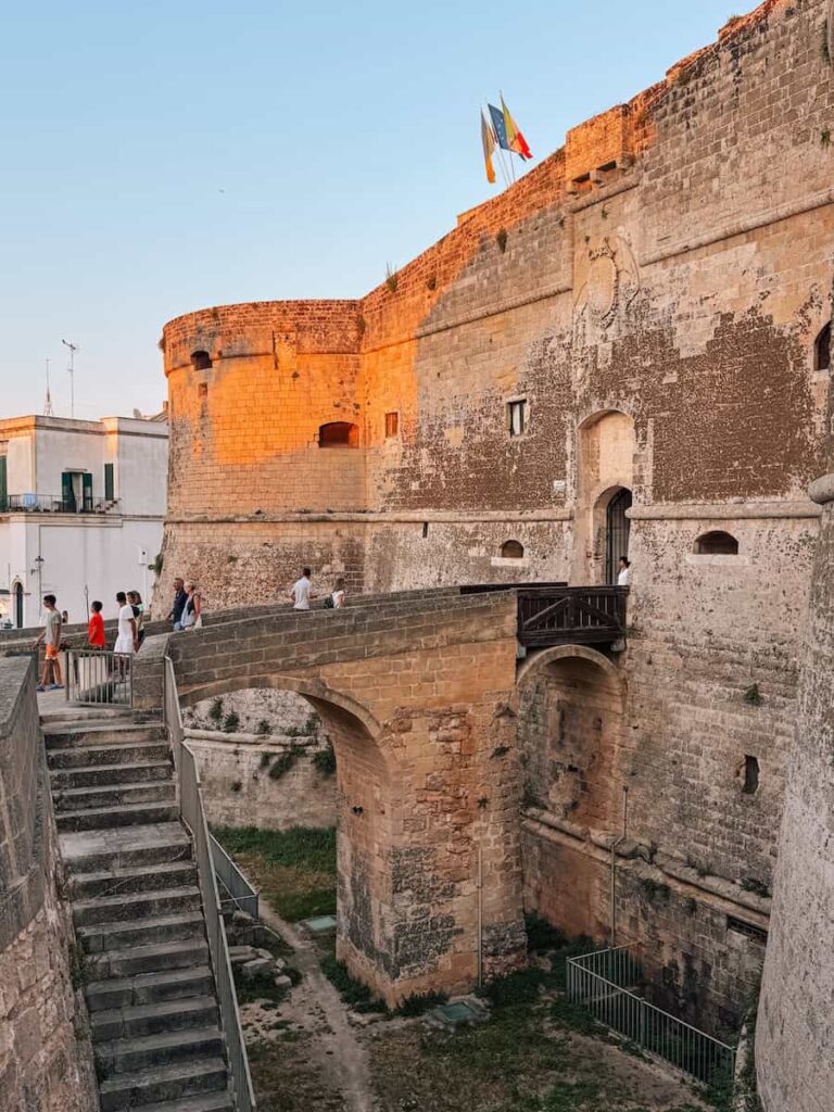 The Aragonese Castle of Otranto at golden hour, featuring its massive stone walls, historic entrance bridge, and impressive medieval fortifications overlooking the old town.