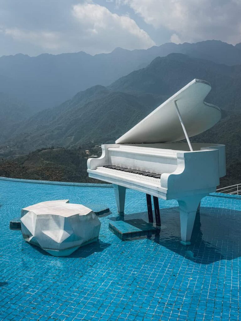 White grand piano set in an infinity pool at Moana Sapa in Sapa, Vietnam, with panoramic mountain views in the background.