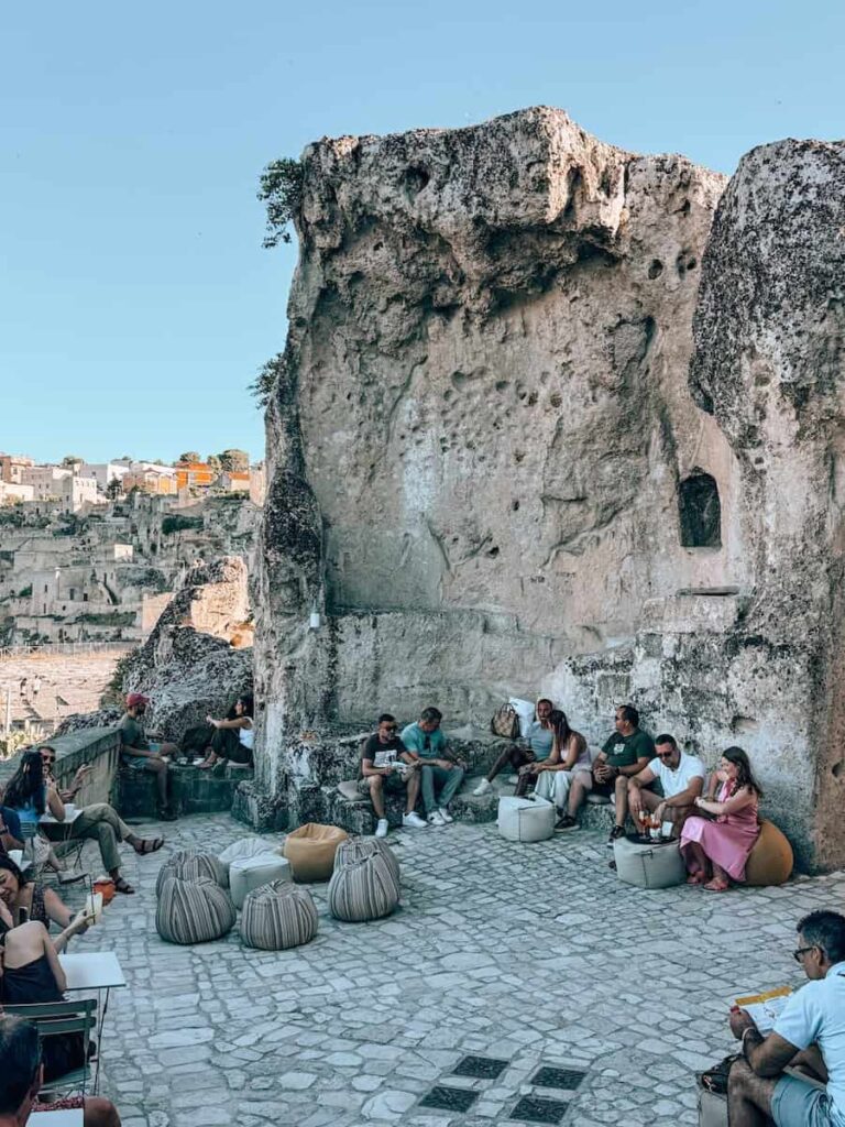 Outdoor seating area at Zipa Café in Matera, Italy, where visitors relax on beanbags and stone benches beside towering limestone cliffs overlooking the historic Sassi district.