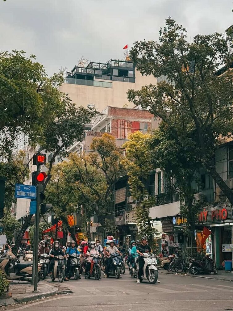 Narrow street lined with shopfronts and scooters in Hanoi's Old Quarter